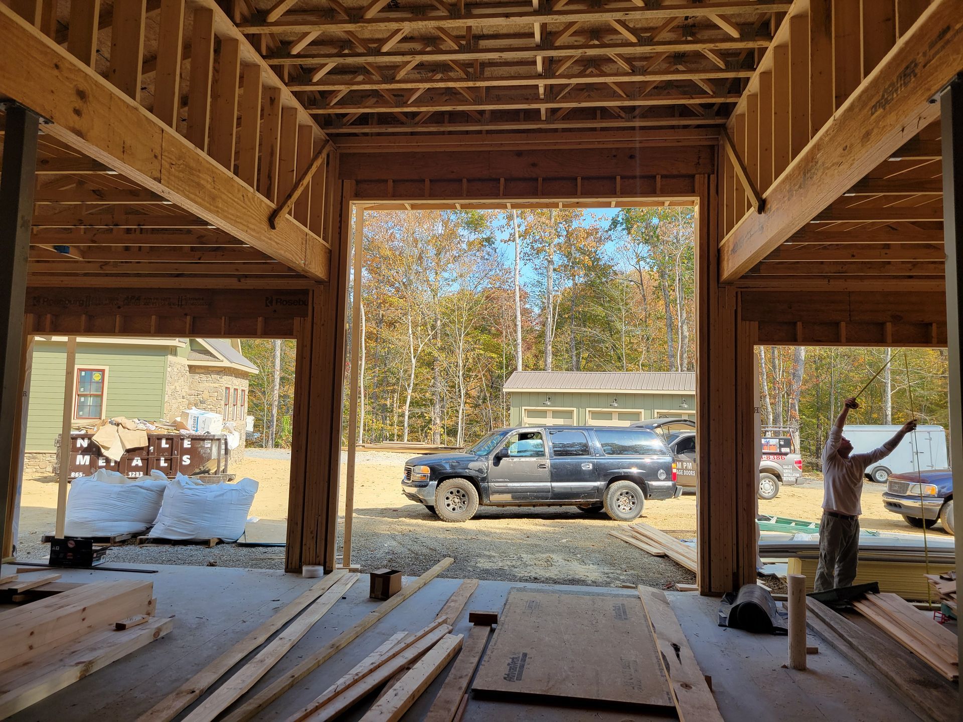 Interior of a wooden barn under construction, with lumber on the floor and a truck visible outside the open entrance.