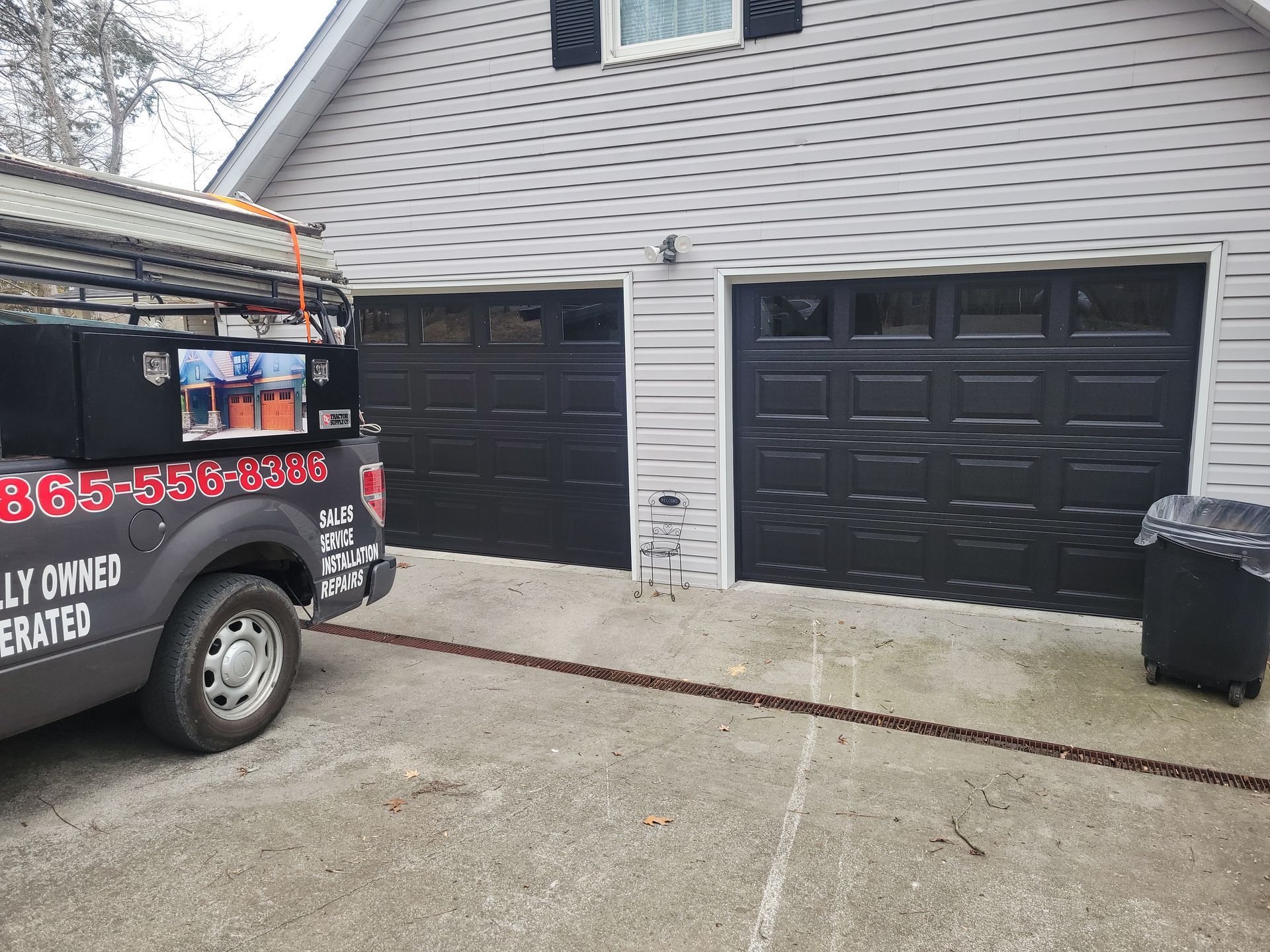 Black double garage doors on a gray house with a van parked in the driveway