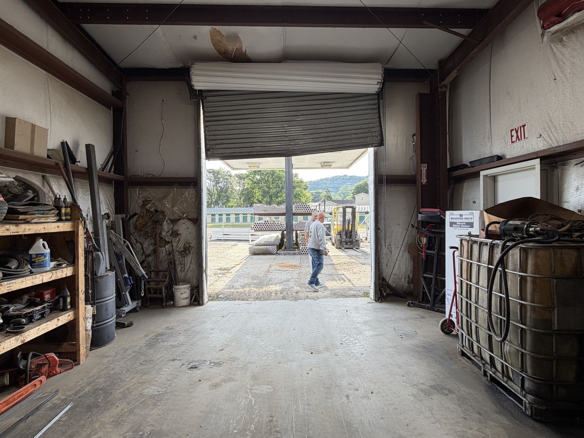 Inside a warehouse bay, a person stands by an open roll-up door with pallets and shelves around them.