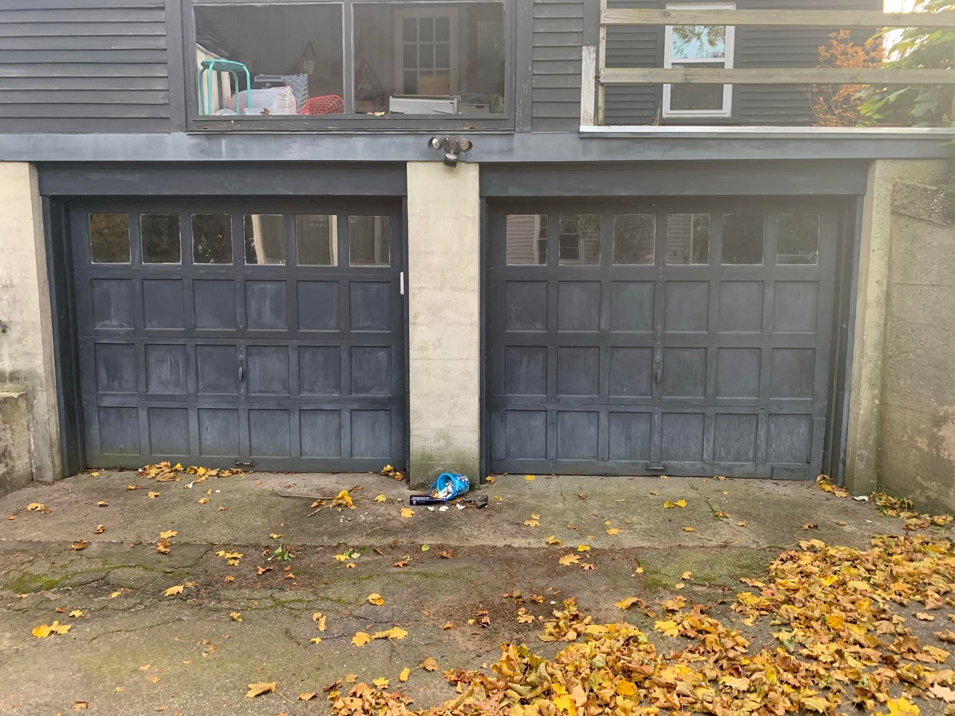 Two black garage doors with a concrete driveway and fallen leaves in front