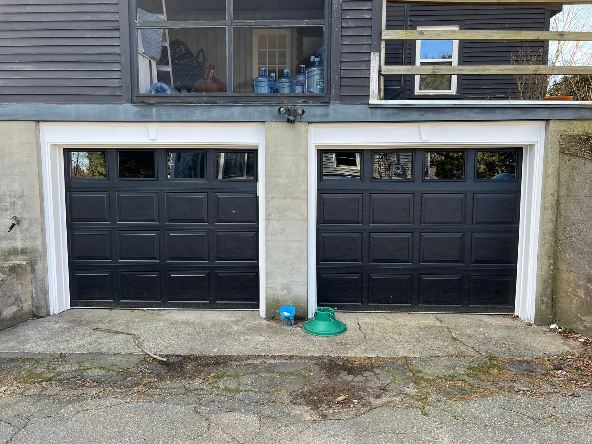 Two black garage doors on a house with white trim and a concrete driveway