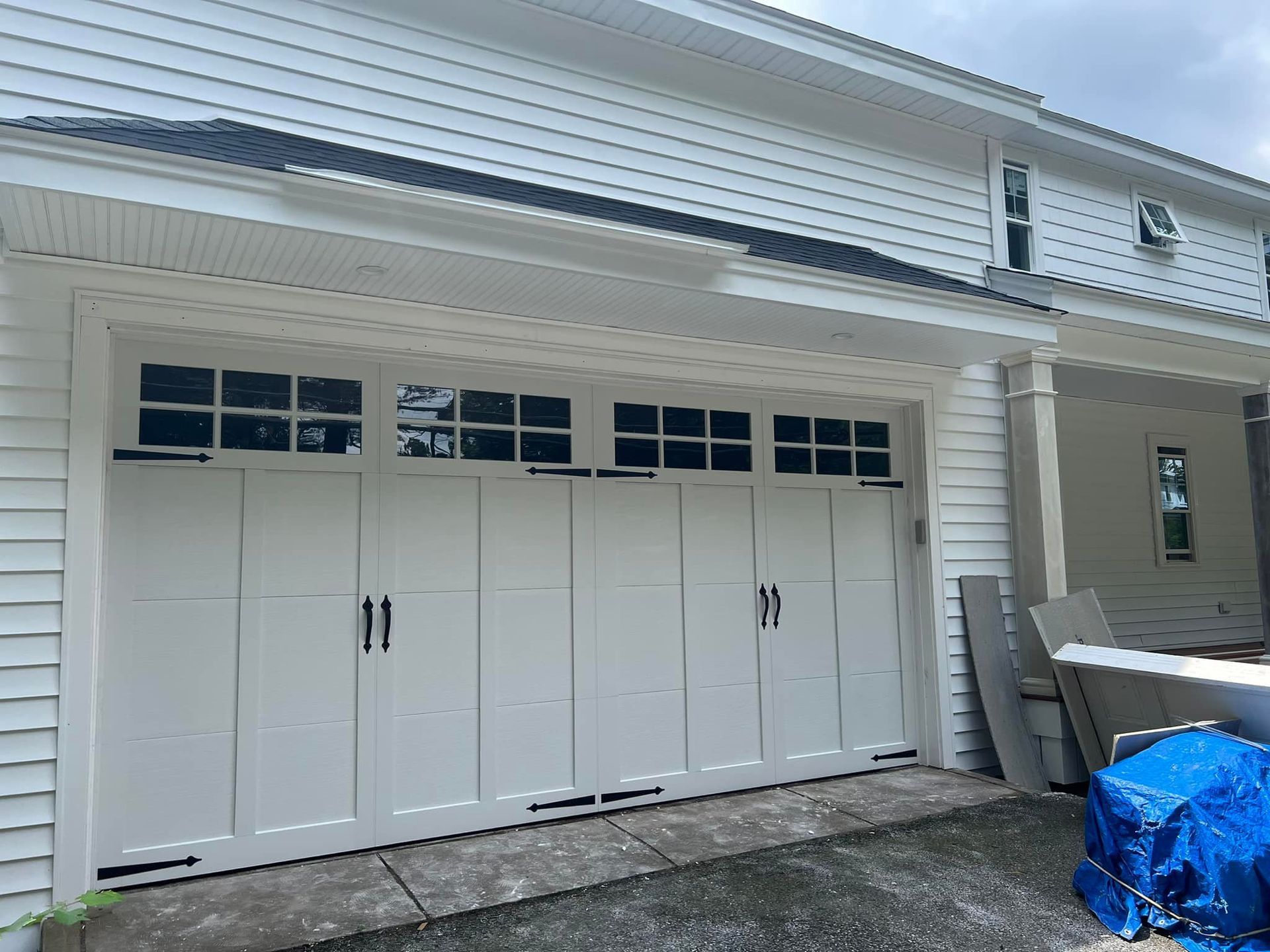 White garage doors on a house exterior with a blue tarp-covered item beside them