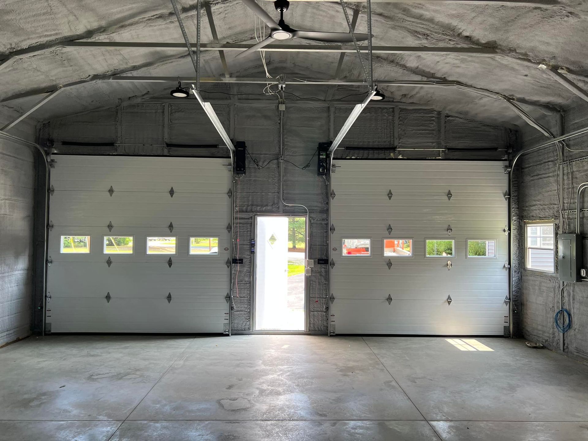 Empty garage with two closed gray doors and a central doorway opening to bright daylight