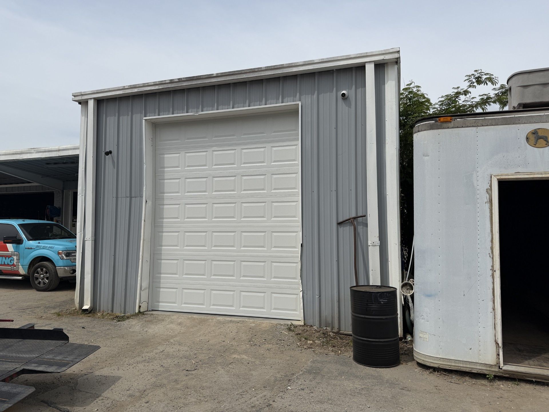 Closed white garage door with red bucket and blue tool on concrete driveway.