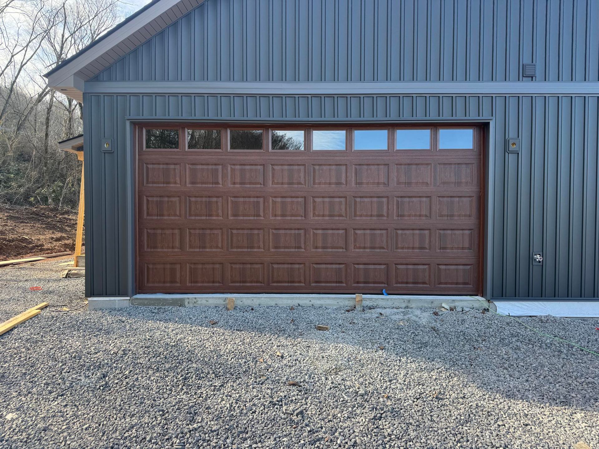 Brown garage door on a dark blue metal building with gravel driveway in front