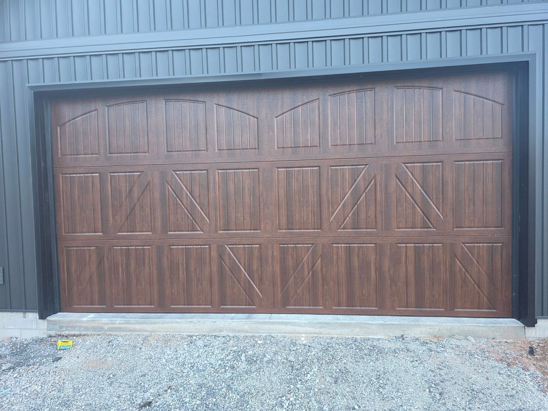 Brown wooden double garage doors on a gray metal building above a gravel driveway