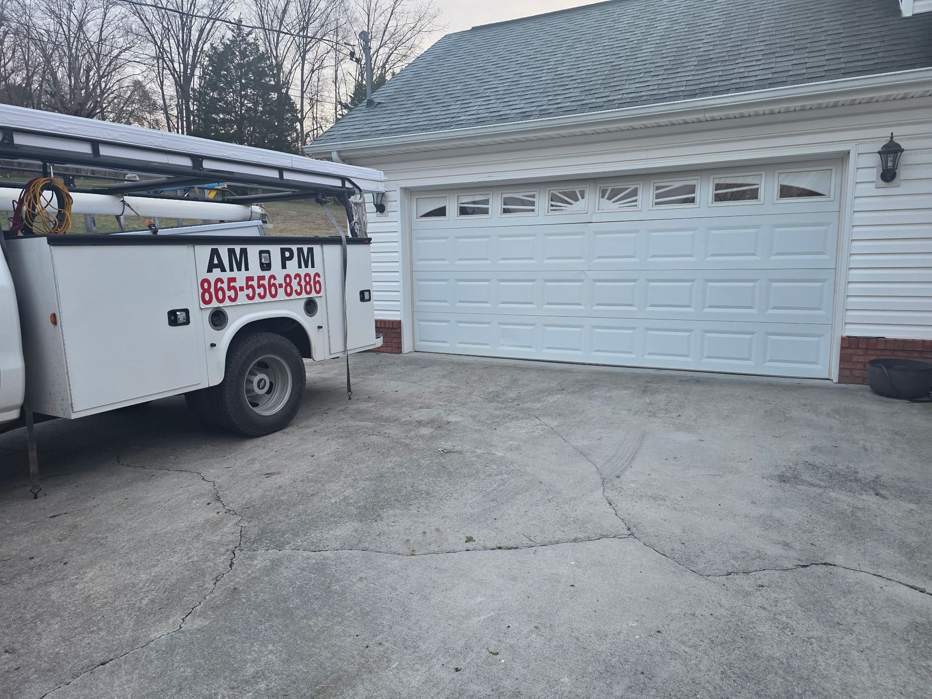Utility truck parked beside a white garage in a driveway on an overcast day