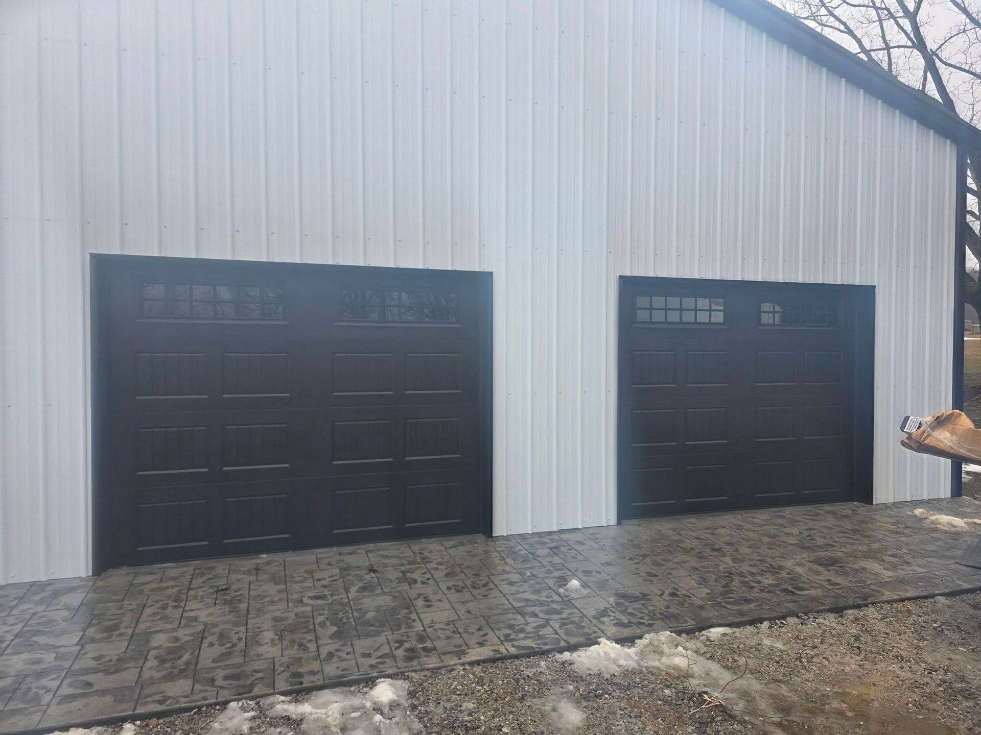 Two black garage doors on a white metal building with a concrete driveway