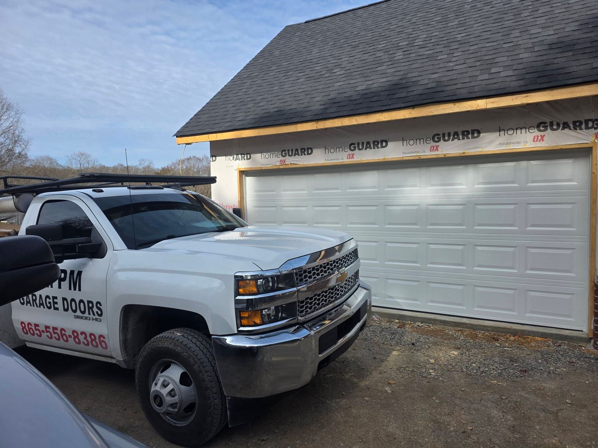 White work truck parked beside a garage with a white door and roof under construction at dusk