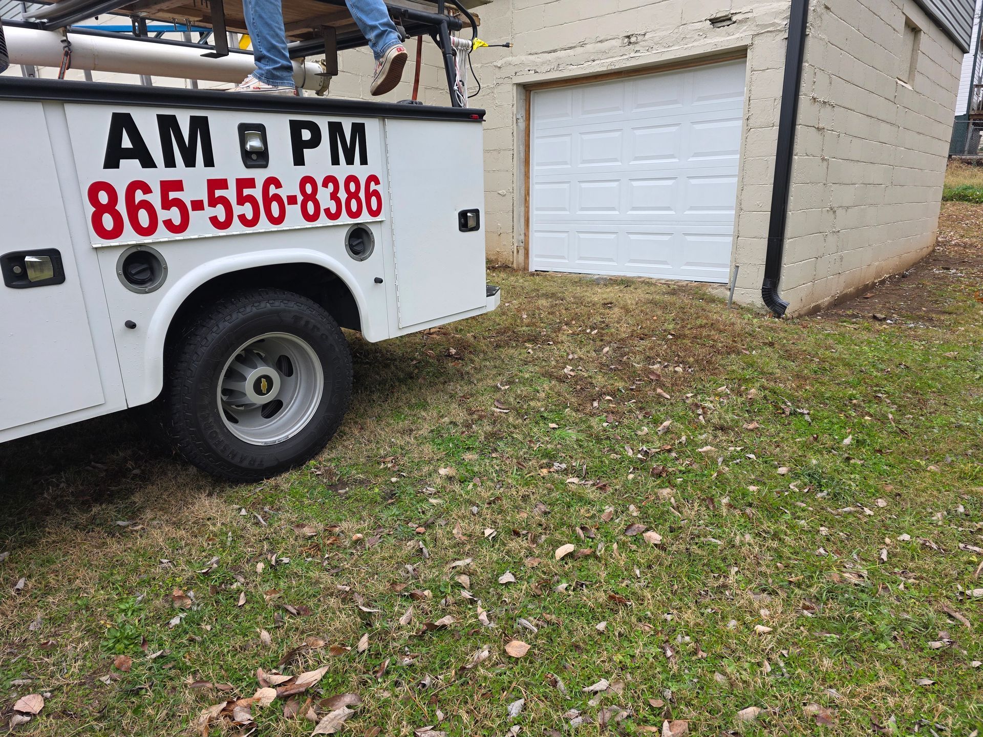 White service truck parked on grass beside a brick house and garage door
