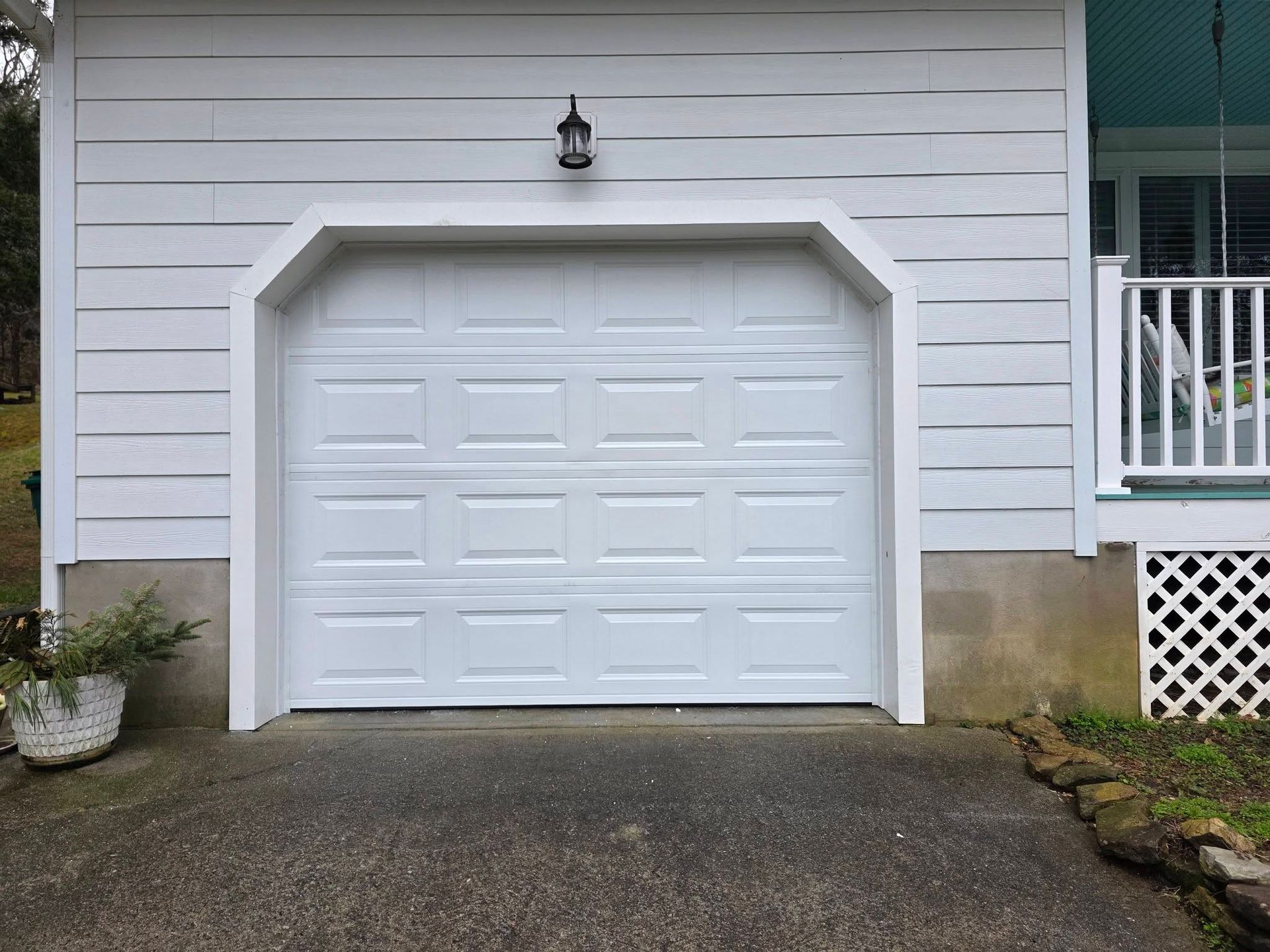 White garage door with decorative trim on a house exterior, beside a porch and driveway.