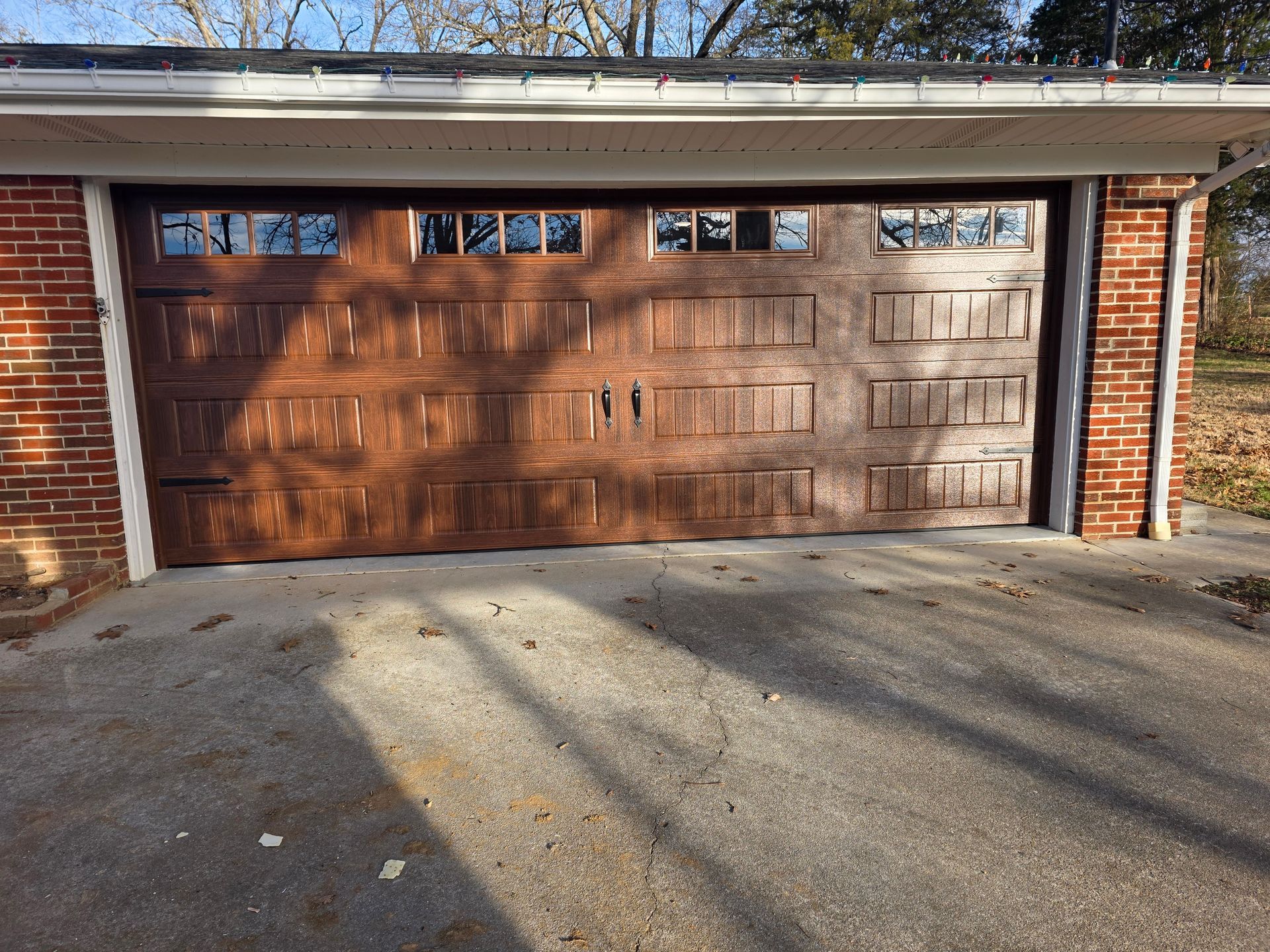 Two-car brown wooden garage door with brick sides and a concrete driveway in front