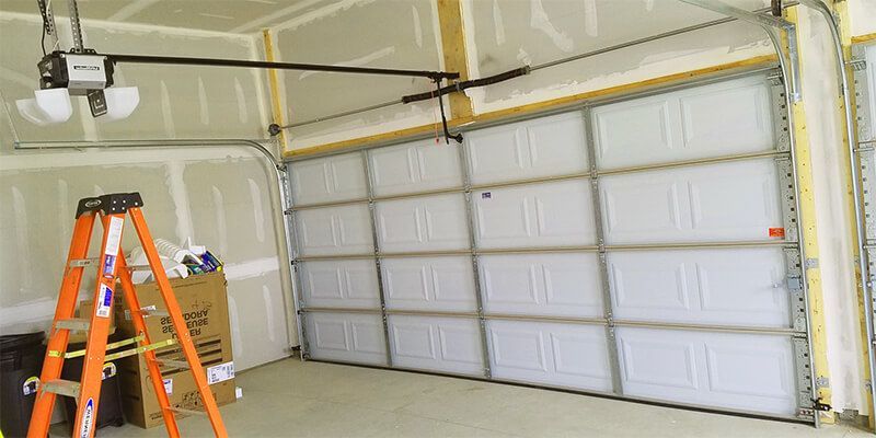 Garage interior with an orange ladder, garage door, and cleaning supplies on the floor.