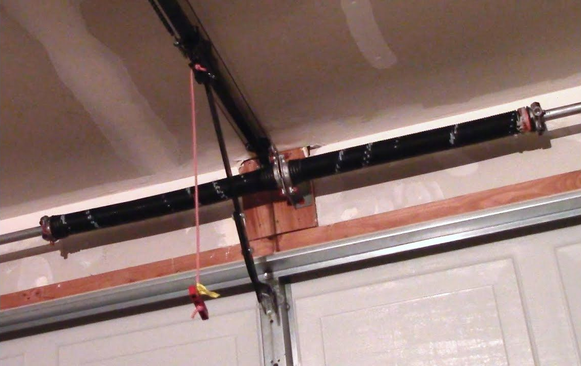 Garage ceiling with a black garage door opener track and a red pull cord hanging down