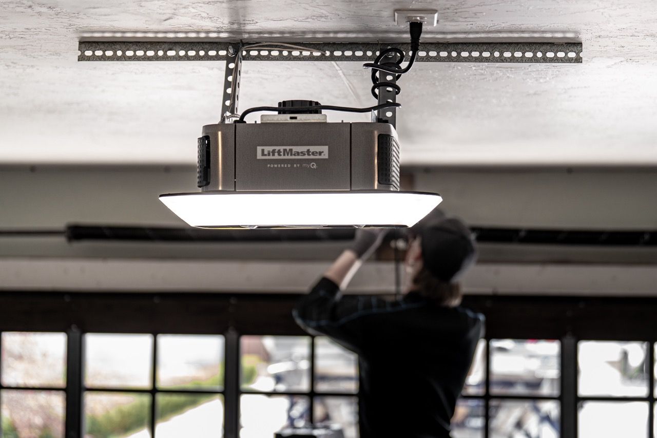 Person adjusting a ceiling-mounted projector in a room with large windows
