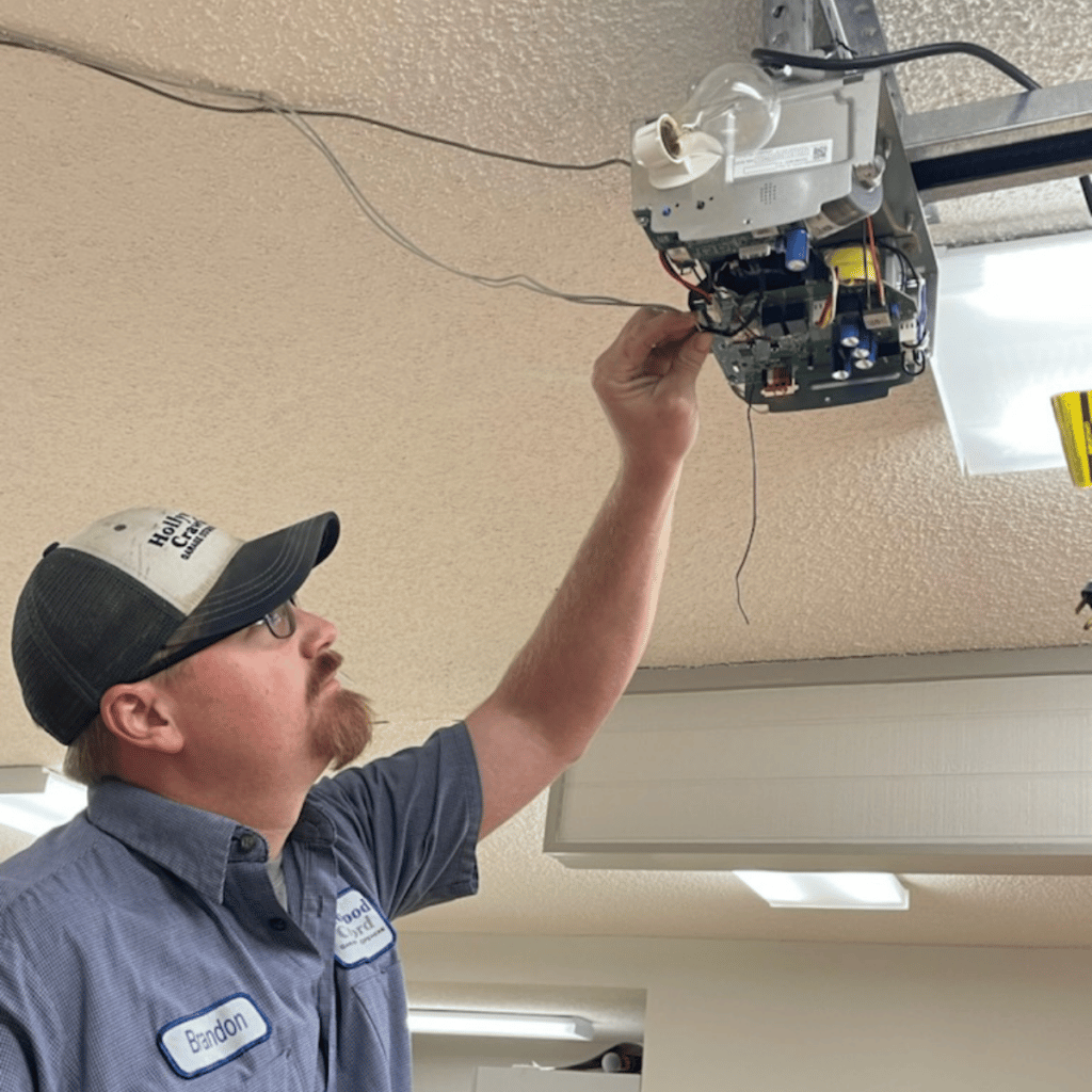 Technician inspecting a ceiling-mounted device with exposed wiring in a room