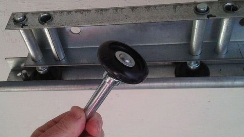 Hand holding a wheel latch against a metal rail bracket with bolts and posts