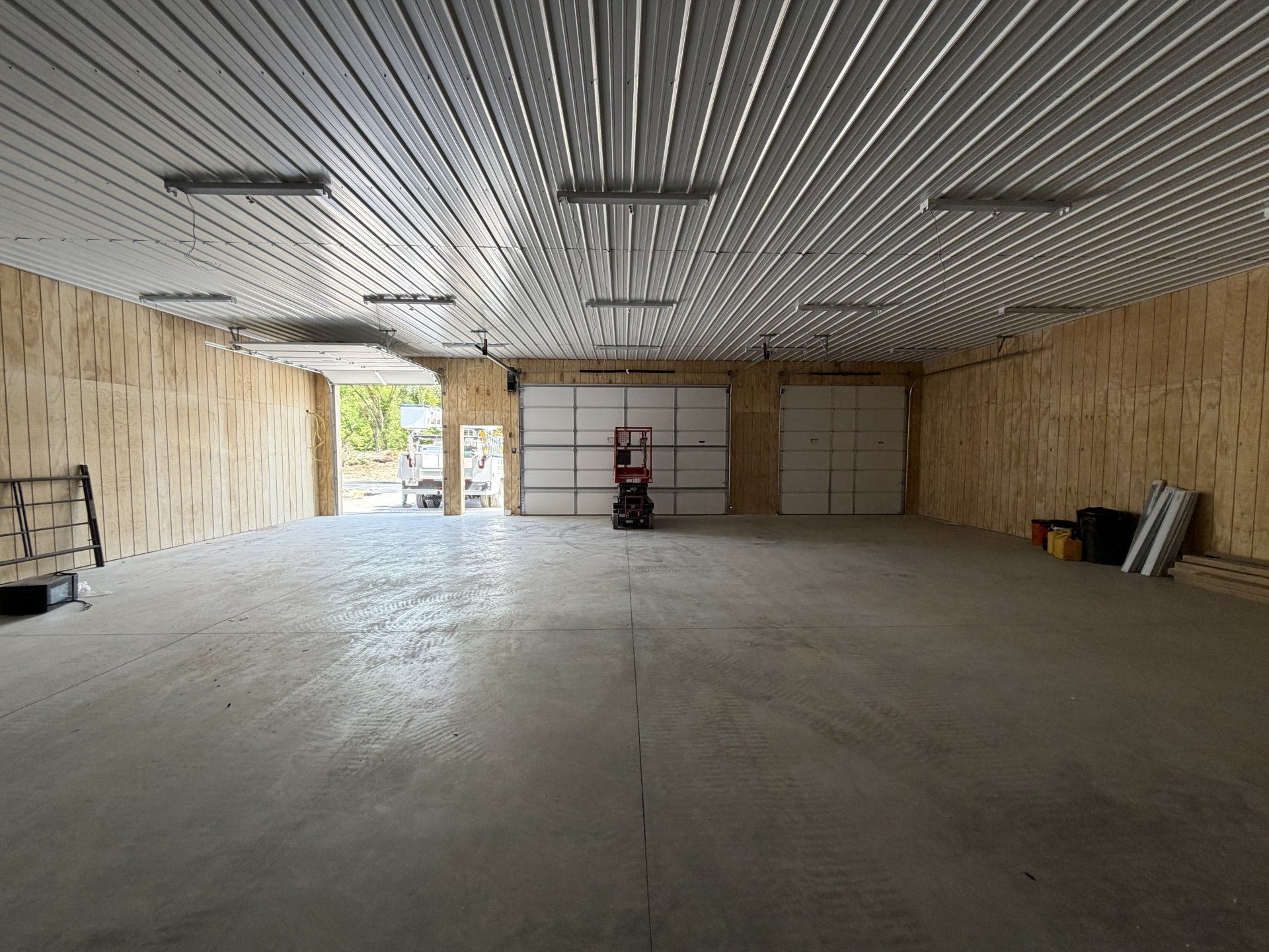 Empty unfinished garage interior with concrete floor, wood-paneled wall, and open doorway letting in daylight