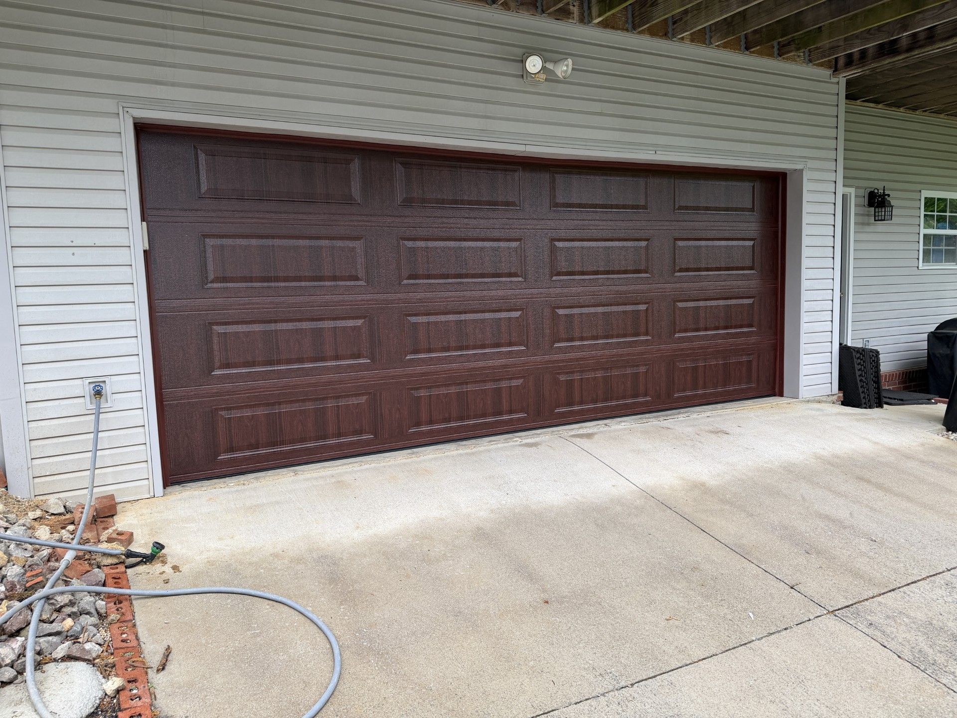 Brown garage door on a white-sided house with a concrete driveway in front
