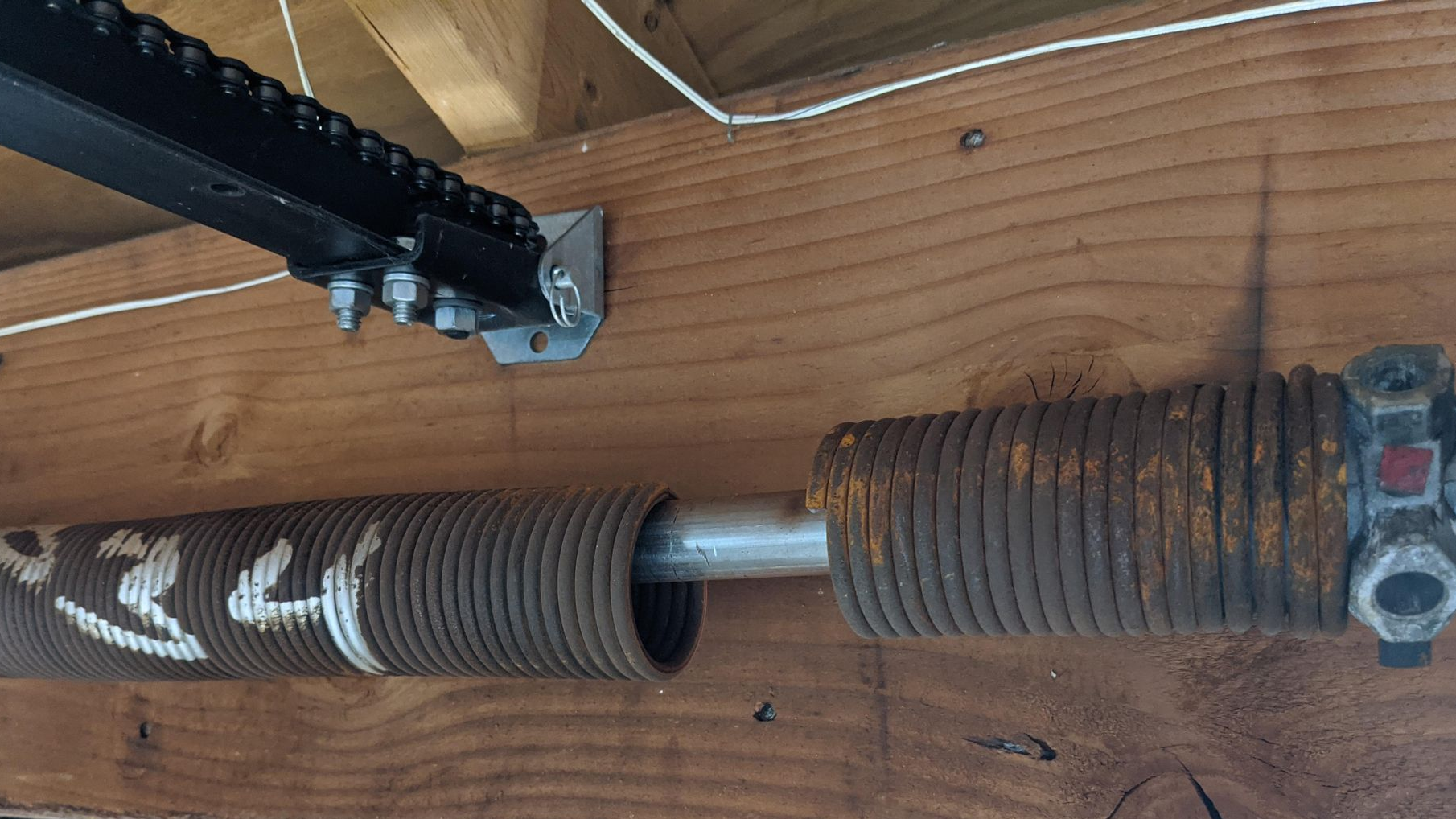 Close-up of a garage door torsion spring with a broken coil and metal shaft on a wooden beam