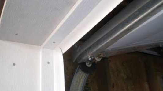 Close-up of a white cabinet hinge and dark metal track inside a drawer or sliding door mechanism