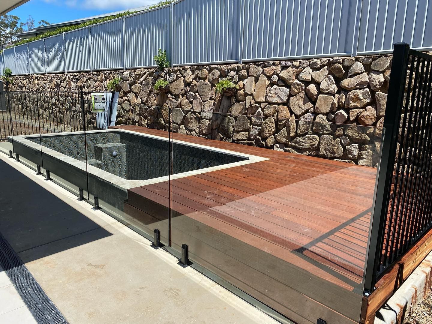 A Swimming Pool Surrounded by a Stone Wall and a Wooden Deck β Swift Glass & Aluminium In Woolgoolga, NSW