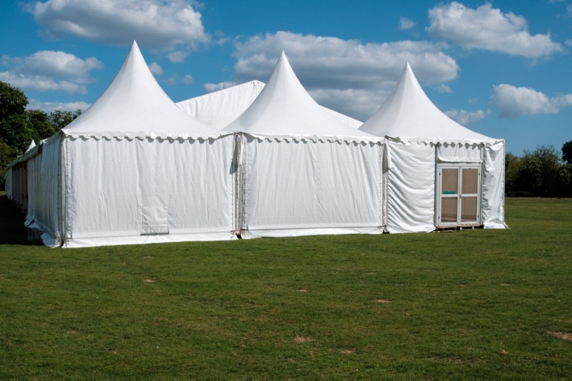 White event tents on a grassy field under a blue sky with clouds