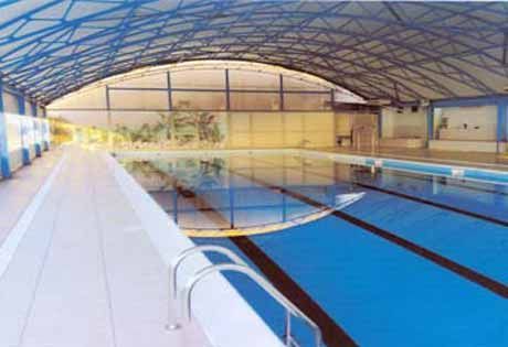 Piscina coperta con corsie blu sotto un tetto curvo, vista dal terrazzo