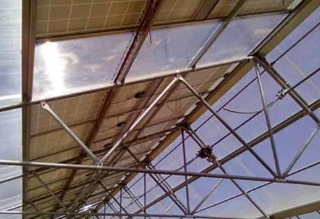 Travi metalliche del tetto e pannelli traslucidi visti dal basso contro un cielo azzurro.