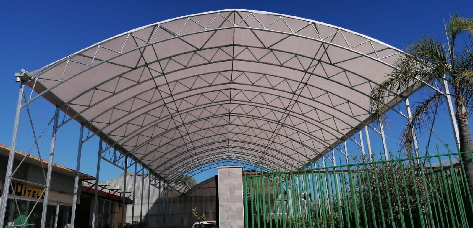 Ampia struttura ad arco con tetto decorato, stagliata contro un cielo azzurro e fiancheggiata da palme.