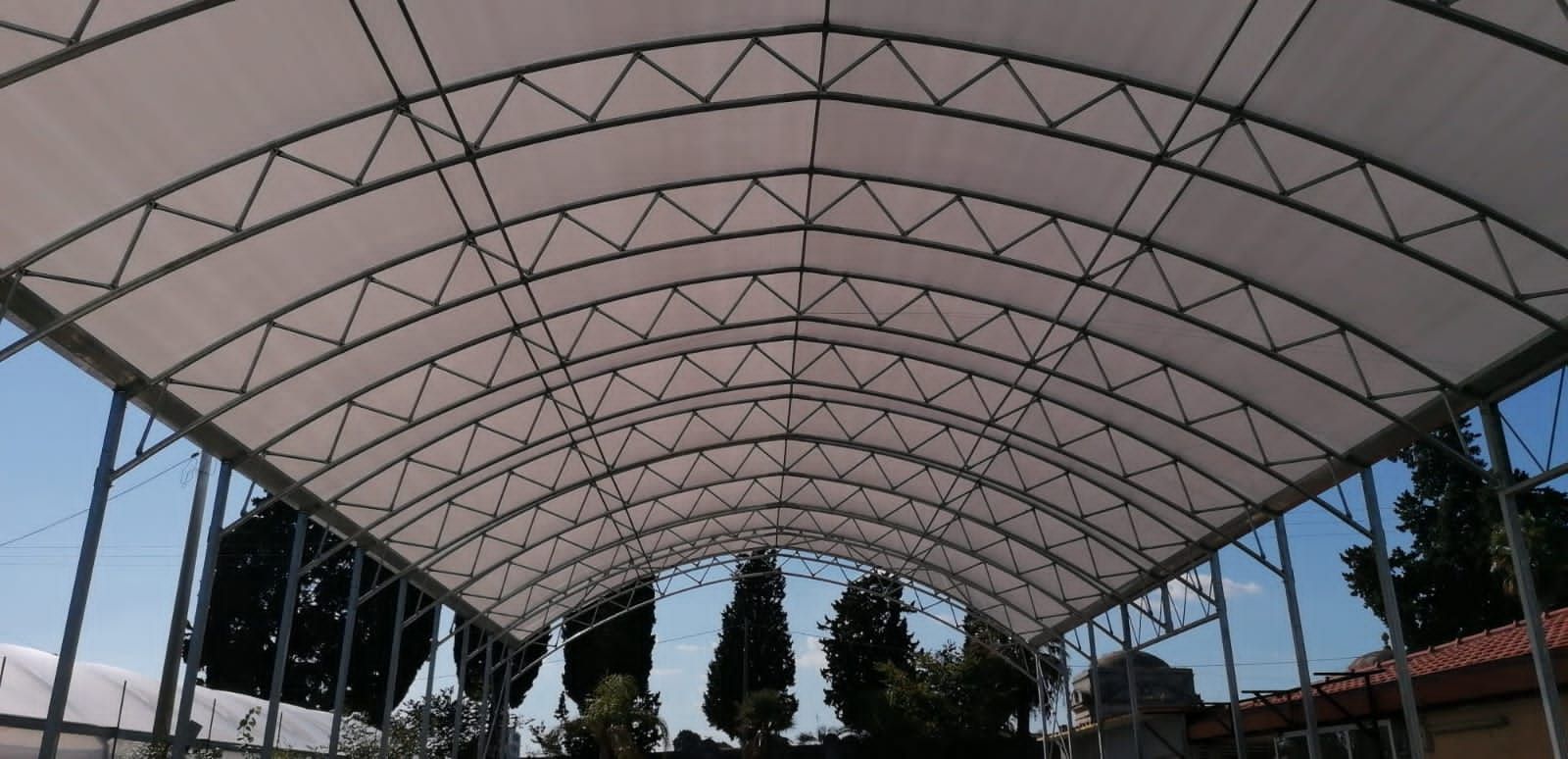 Padiglione esterno coperto con tetto ad arco bianco e alberi sullo sfondo.