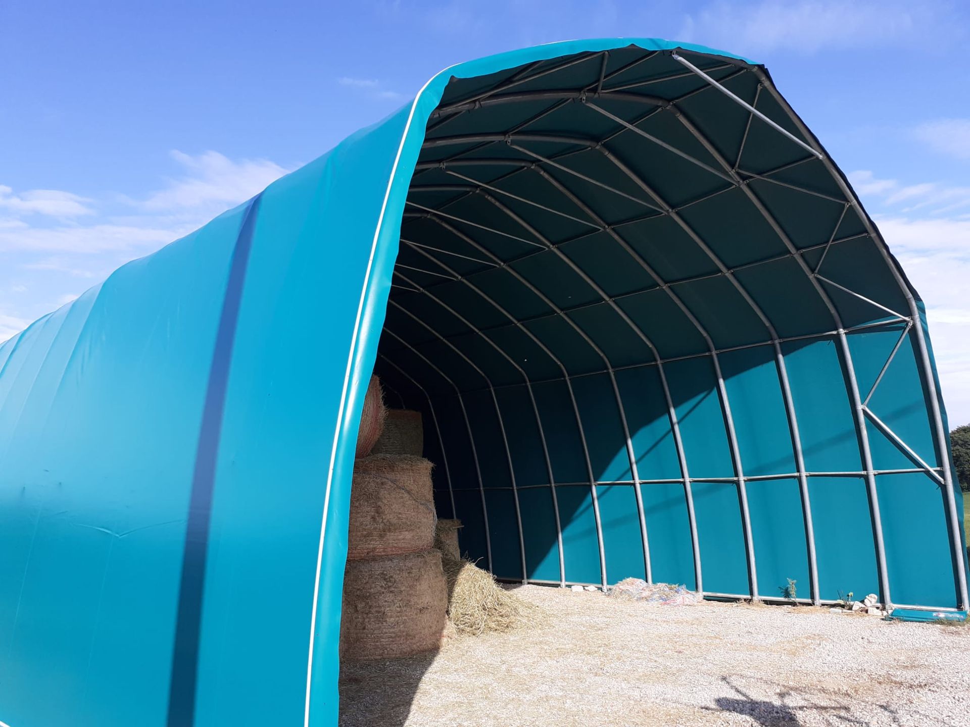 Riparo agricolo coperto da un telone blu con fieno all'interno, aperto in un campo.