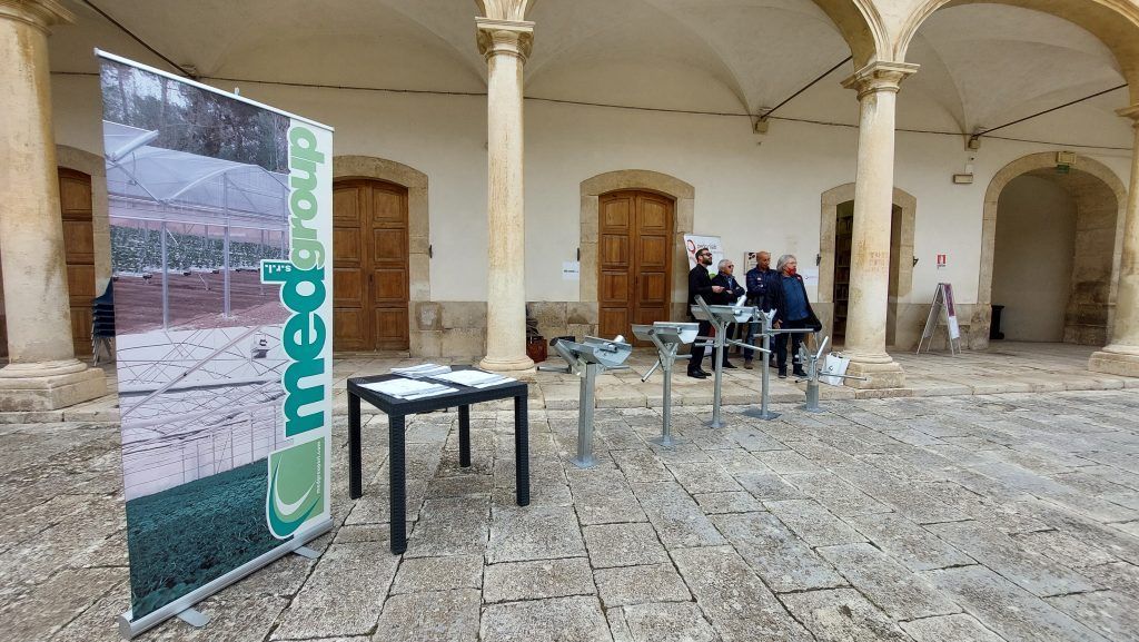 Cortile interno con pavimento in pietra, porte ad arco, tavoli e un alto stendardo in primo piano.