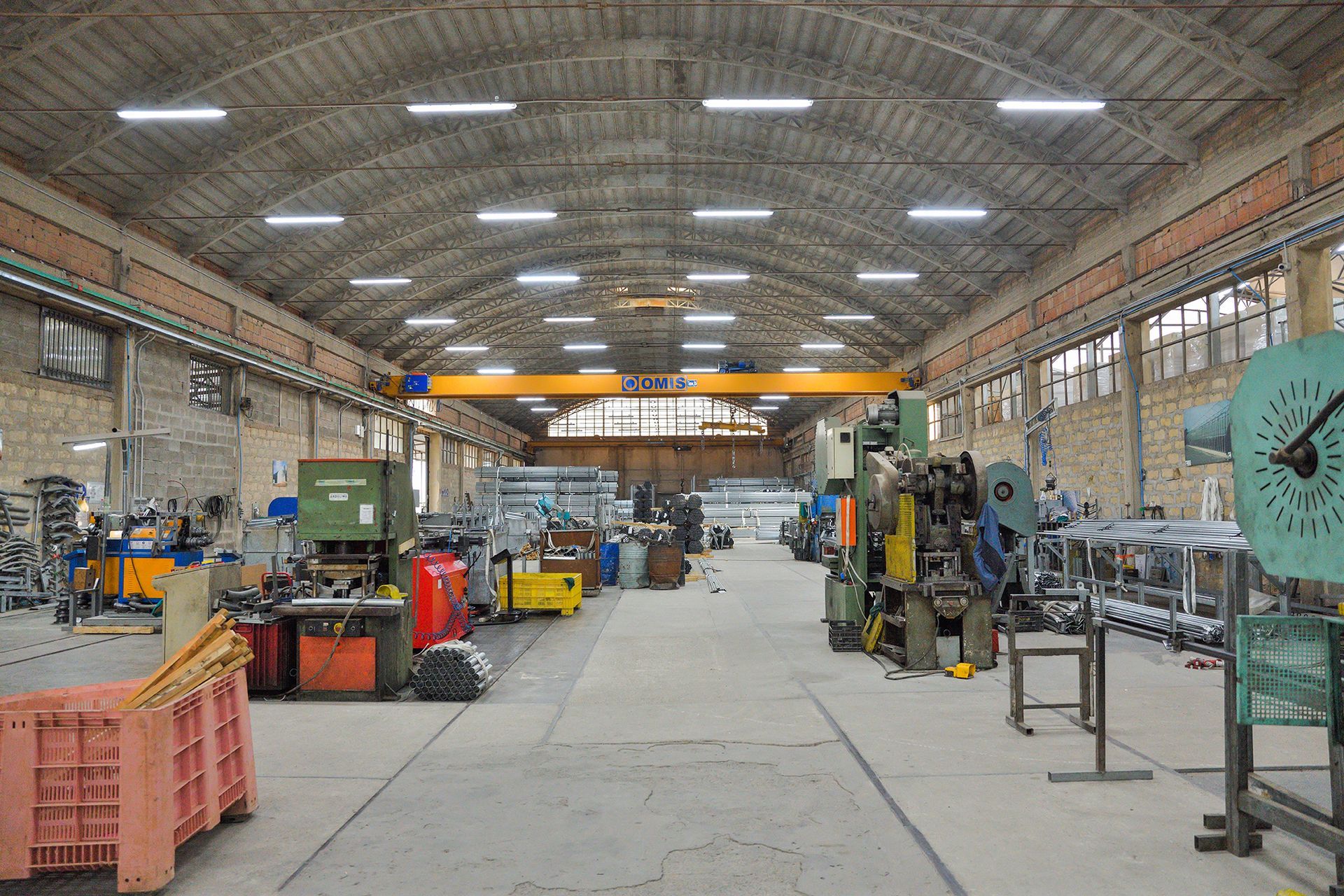 Interno di un'officina industriale con macchinari, utensili e luci a soffitto in un ampio spazio di lavoro con pavimento in cemento.