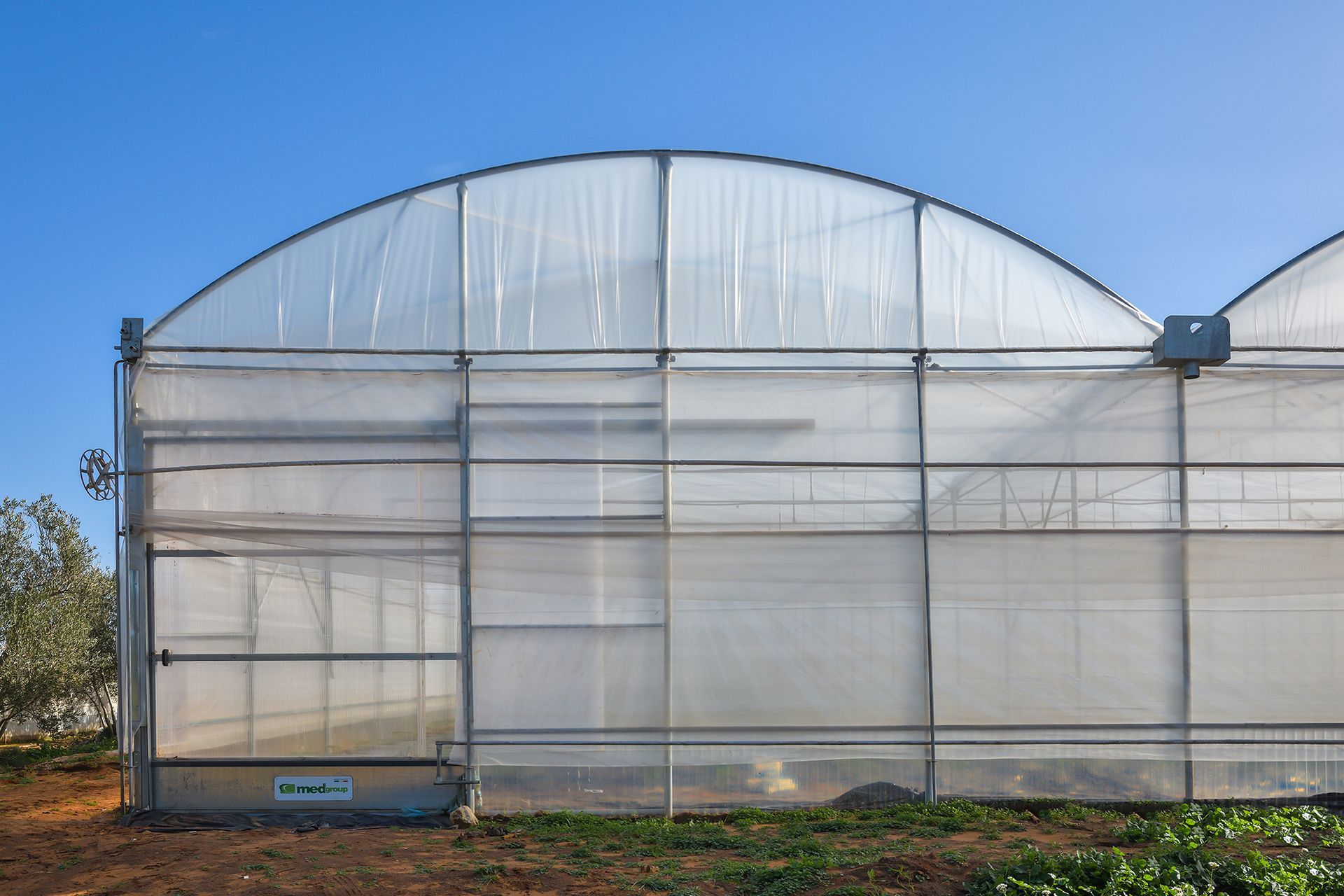 Grande serra ad arco con pannelli di plastica traslucida in un campo rurale sotto un cielo azzurro