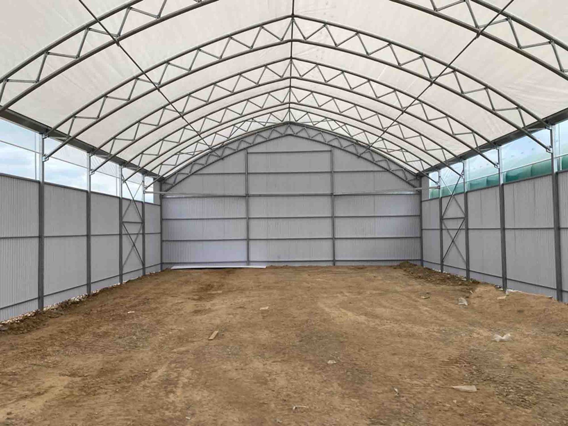 Serra ad arco vuota con pavimento in terra battuta e pannelli laterali traslucidi.