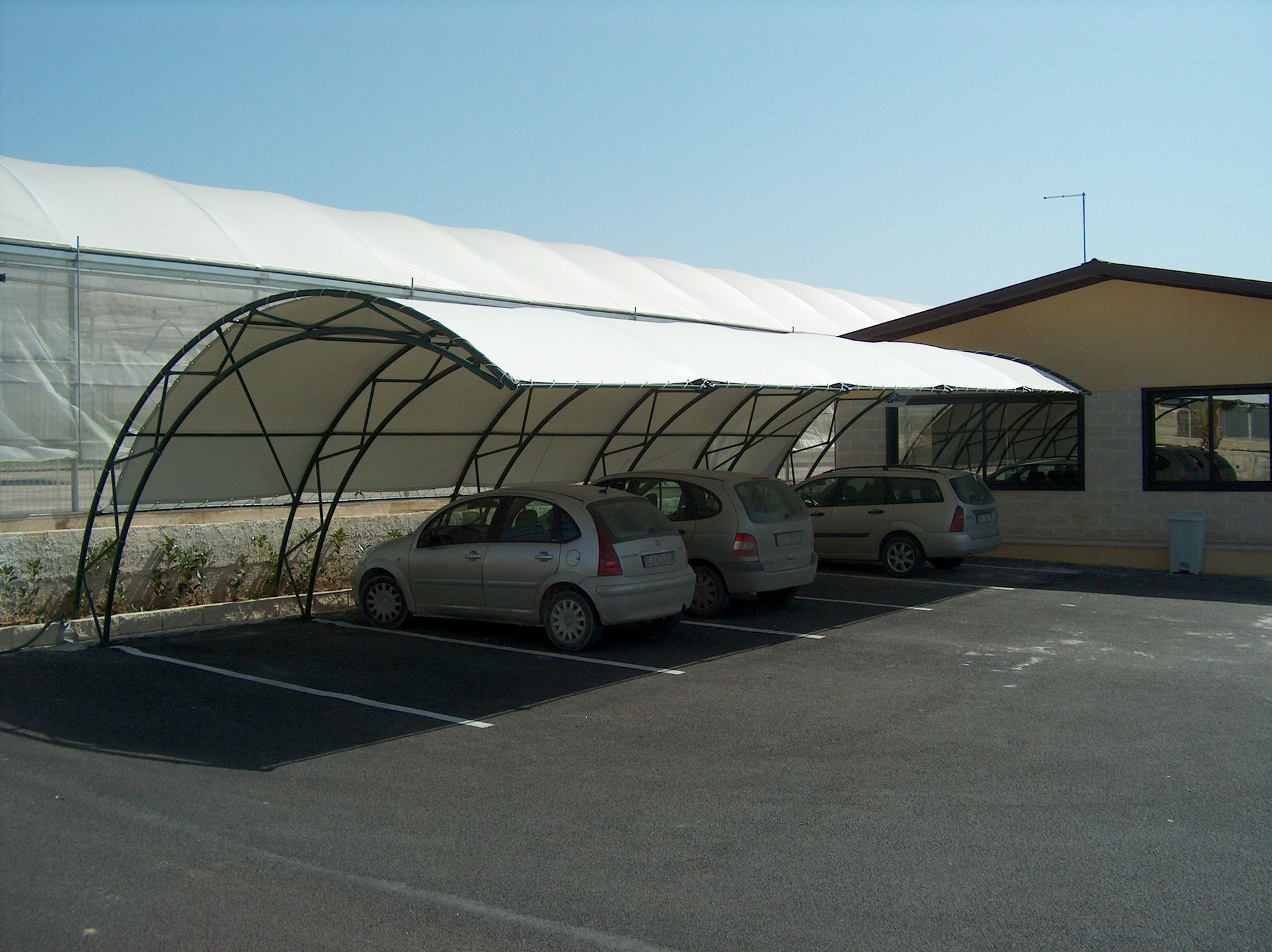 Parcheggio coperto con tre posti auto accanto a un edificio beige.