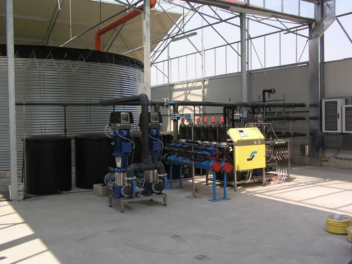 Officina industriale con tubature blu, un macchinario giallo e serbatoi metallici in un ampio spazio industriale.