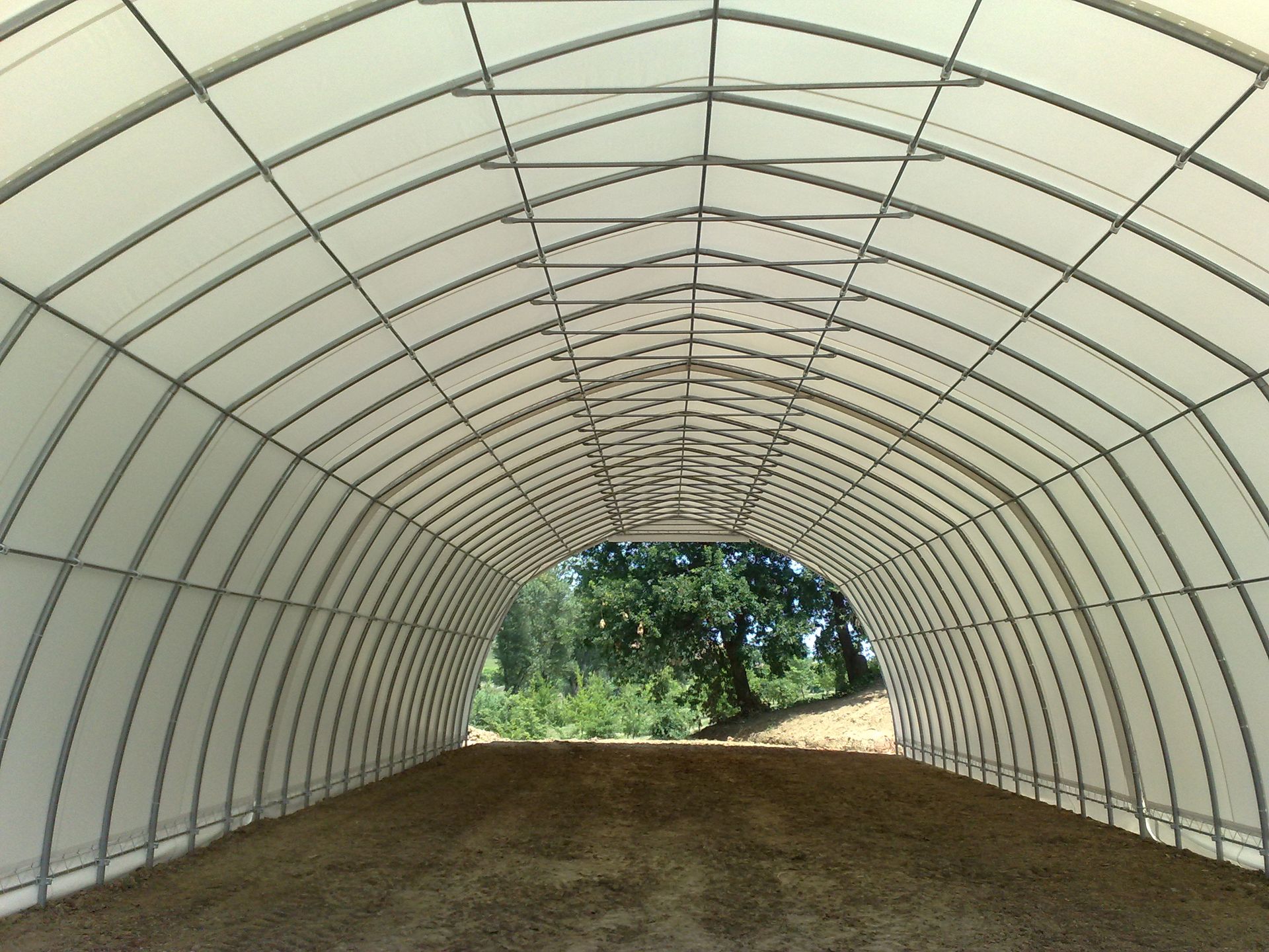 Tunnel ad arco vuoto con pareti bianche e pavimento in terra battuta che si apre sul verde esterno.