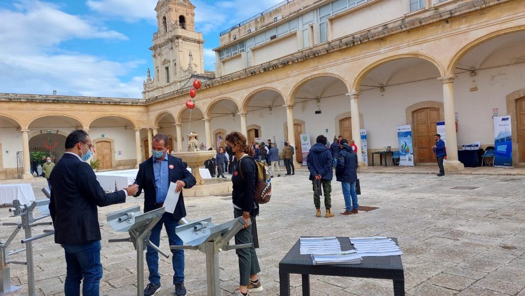 Persone in piedi in un cortile soleggiato accanto a un edificio storico riccamente decorato e a una torre.