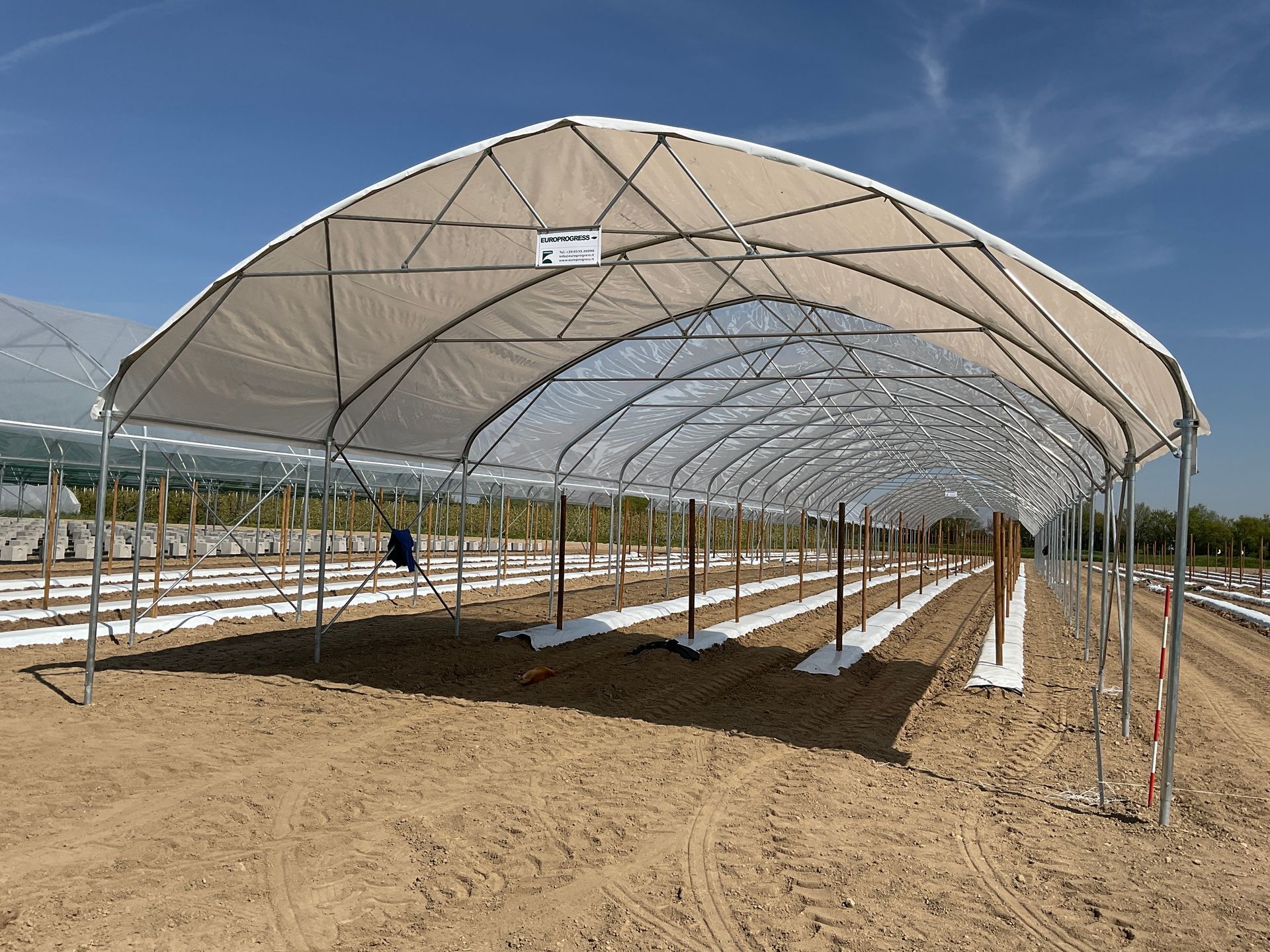 Filari agricoli coperti sotto un grande tunnel ombreggiante in un campo sabbioso