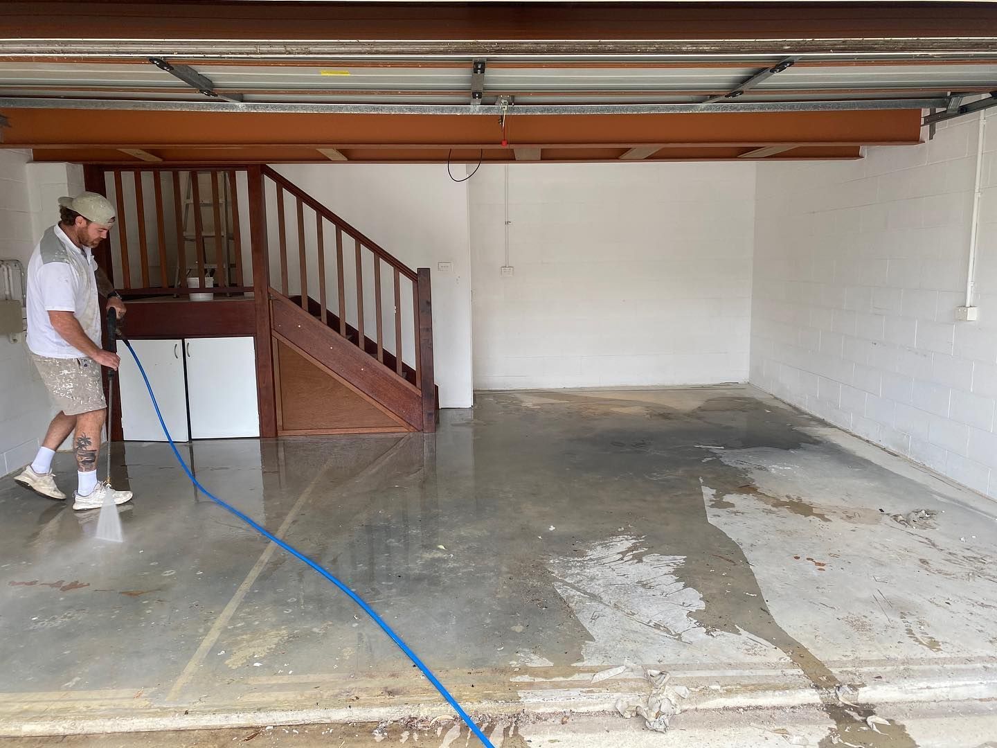 A Man With Hose Washes Garage Floor, Stairs in Background — All Coast Painting in Tweed Heads South, NSW