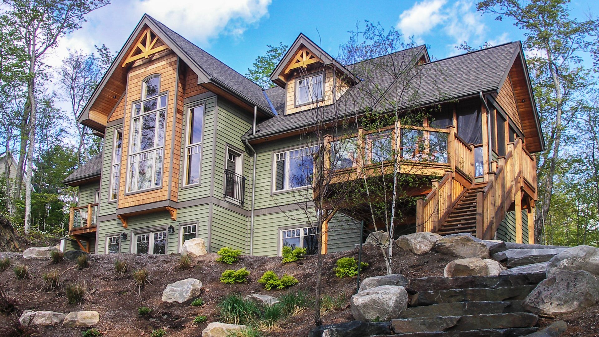 View of a multi-storied home on a rocky hill, with exposed wooden beams and matching shingle design.