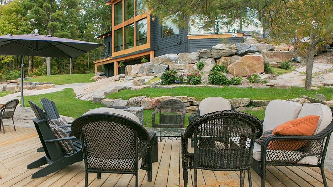 Wooden deck with deck chairs outside of a modern cottage. Large rocks and cottage in the background, 