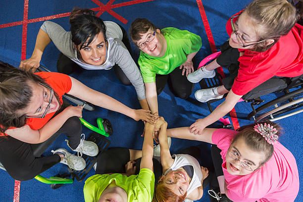 A group of children in wheelchairs are putting their hands together in a circle.