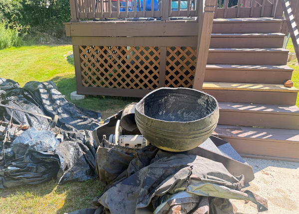 Backyard deck with stairs, a lattice skirt, and a decorative bowl on rocks and landscaping fabric
