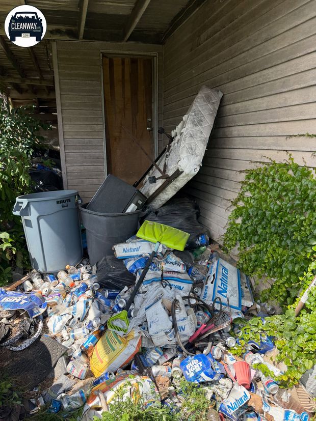 Overflowing trash bags and debris piled beside a house exterior wall and door.