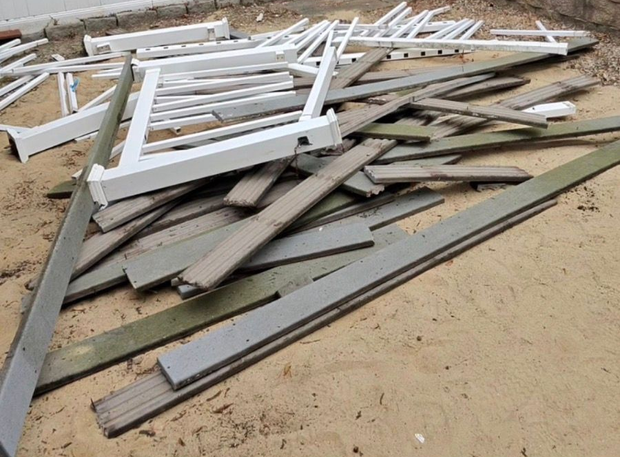 Pile of broken white and gray wooden boards scattered on sandy ground.