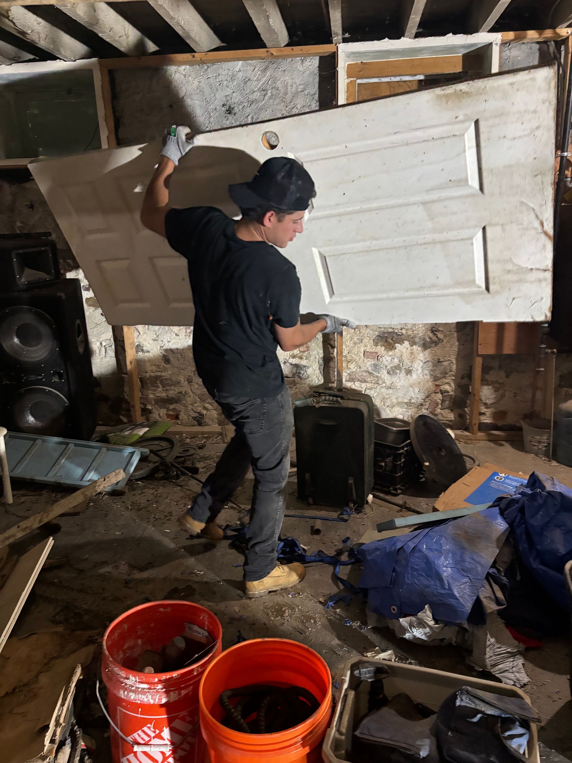 Person painting a white door in a cluttered workshop, with orange buckets and tools on the floor.