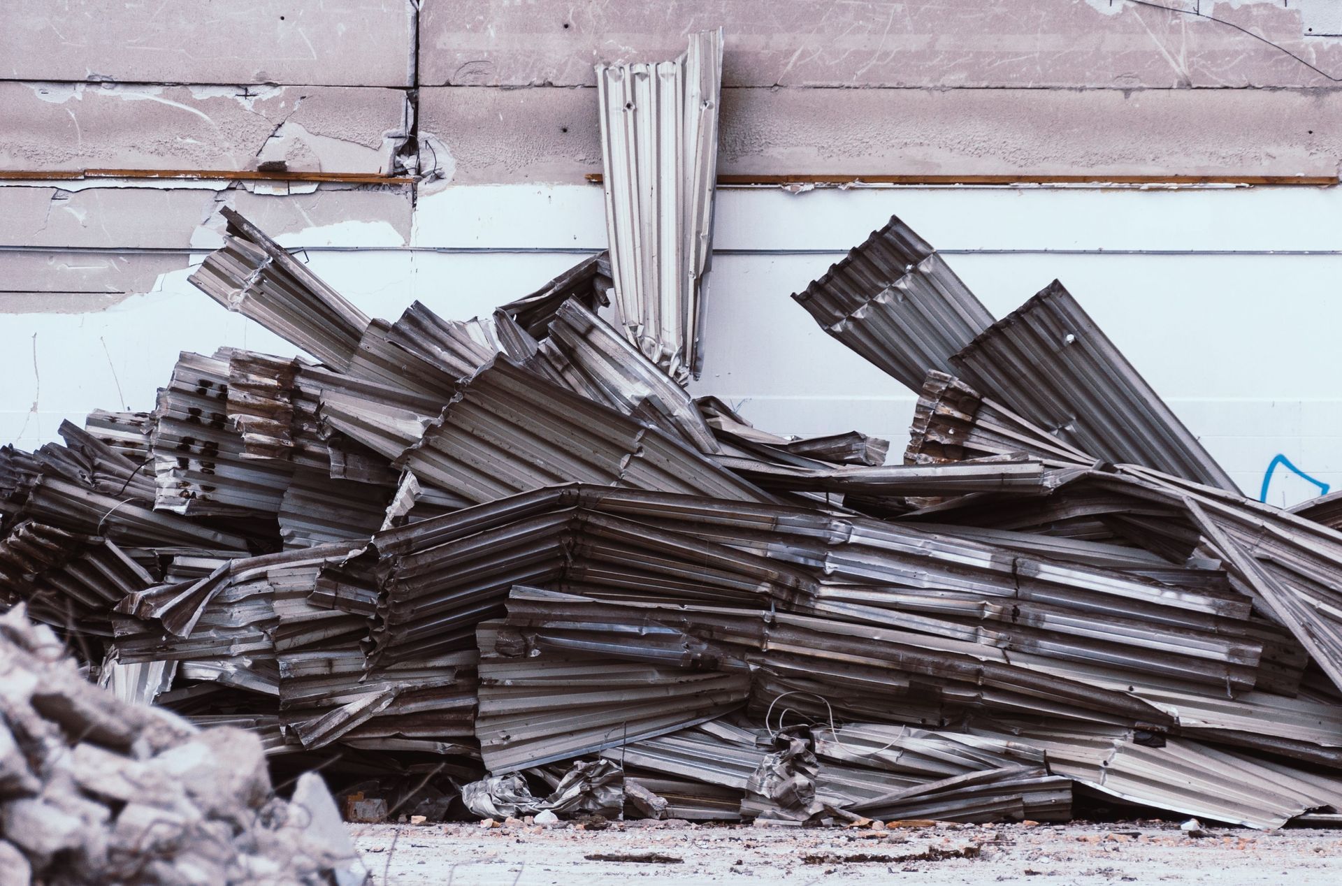 Piled corrugated metal sheets stacked against a weathered wall